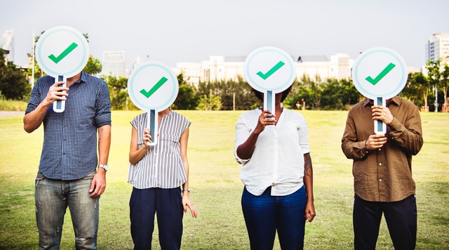 four people holding signs with a green checkmark over their face